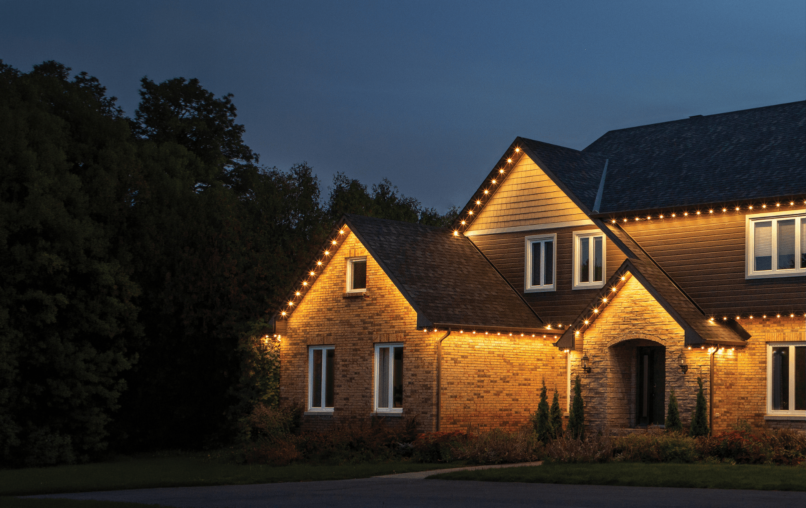 Permanent Christmas lighting along the rooflines of a brick home, installed by Voltex Systems